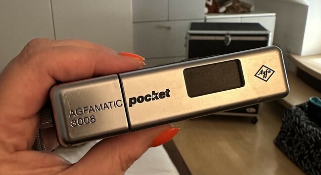 Eine Agfa Agfamatic Pocket 3008 Kamera. Quaderförmig, etwa so groß wie ein altes Nokia Handy. Silberfarbenes Metall und schwarzes Plastik. 