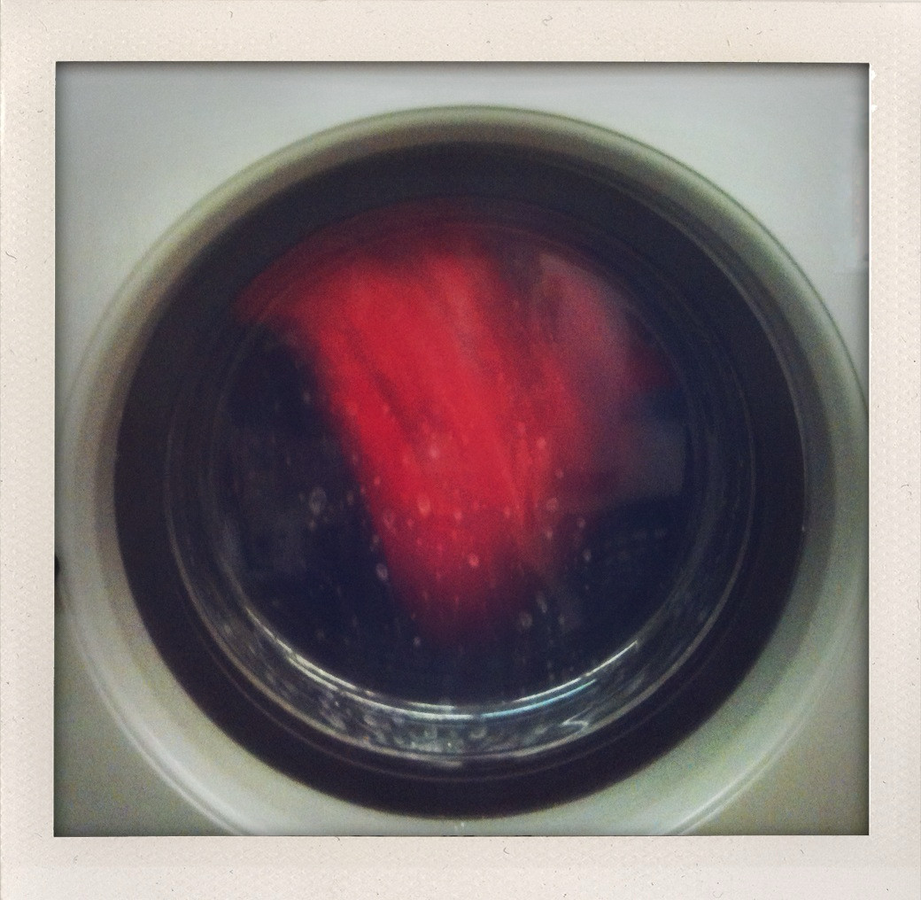 Quadratisches Farbfoto mit Rand, wie bei früheren Polaroidfotos, zeigt das „Bullauge“ einer laufenden Waschmaschine, in der ein rotes Kleidungsteil umeinander wirbelt. Quadratisches Farbfoto mit Rand, wie bei früheren Polaroidfotos, zeigt das „Bullauge“ einer laufenden Waschmaschine, in der ein rotes Kleidungsteil umeinander wirbelt.