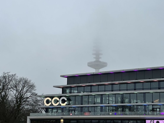 Vorderansicht des CCH, derzeit als CCC beschriftet. Im Hintergrund verliert sich der Fernsehturm im Hochnebel. 